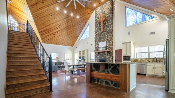 A spacious interior with a wooden staircase, a stone accent wall, and a kitchen area.