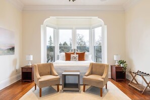 Ein Schlafzimmer mit großem Fenster, einem Bett, zwei Stühlen, einem kleinen Tisch und Nachttischen.