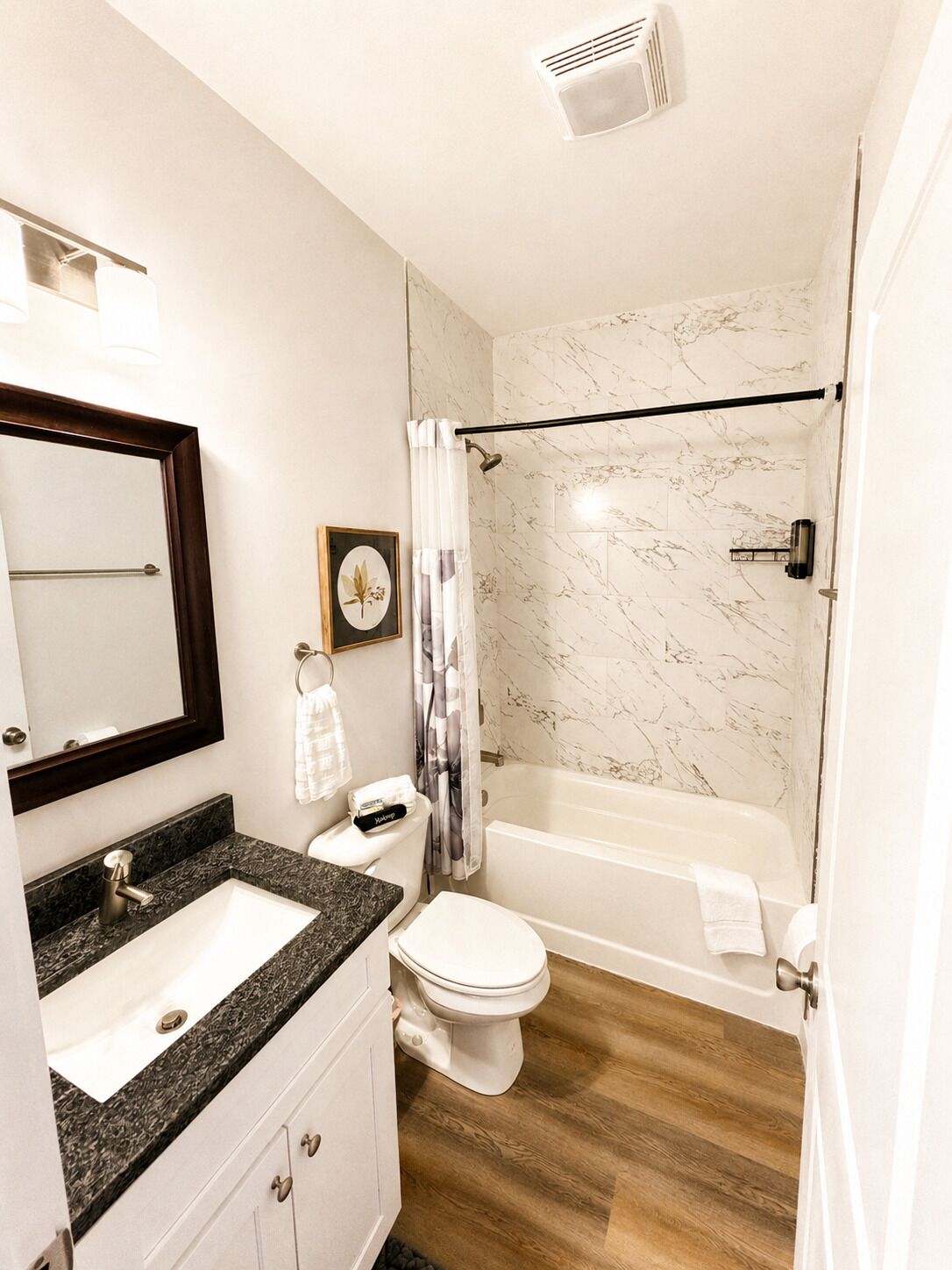 A bathroom with a marble shower, a sink with a marble countertop, a toilet, and a mirror with a wooden frame.