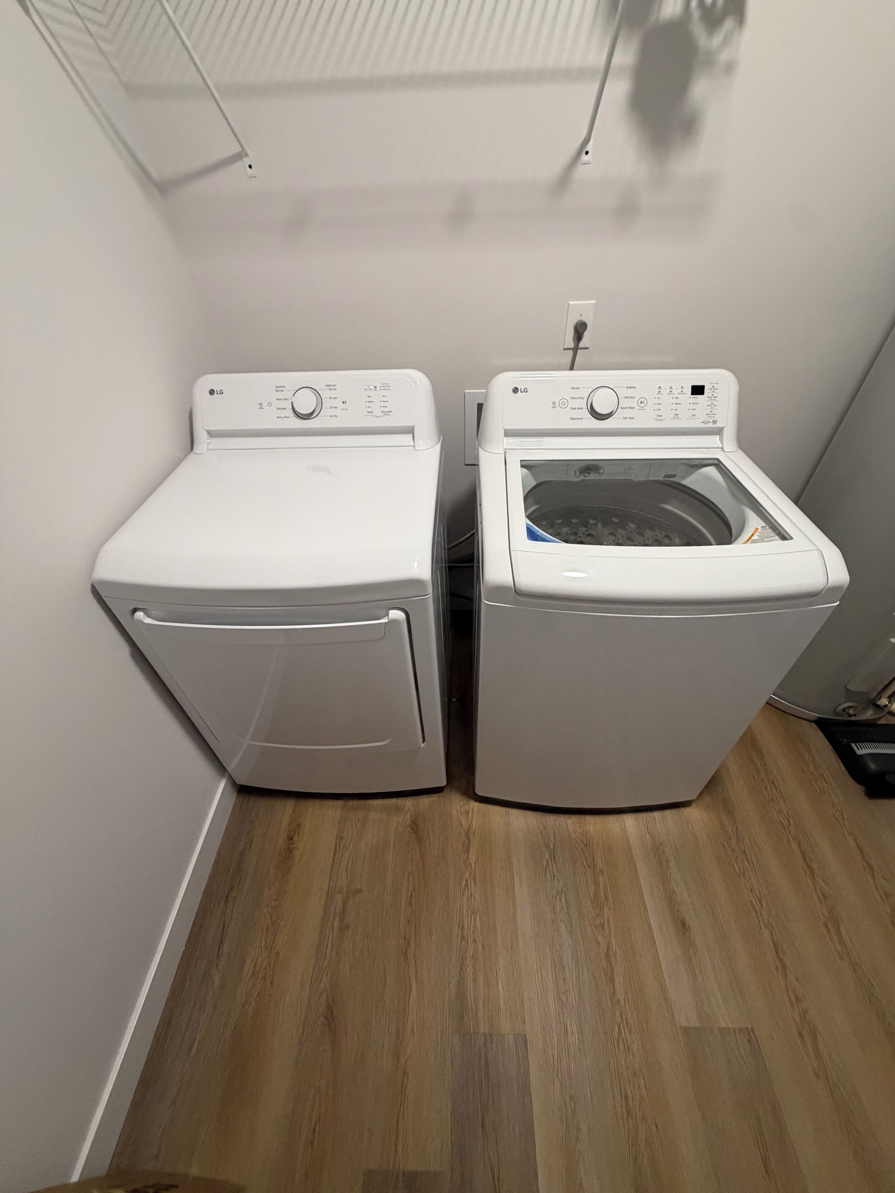 Une buanderie avec deux machines à laver blanches et un sèche-linge, un plancher en bois et un mur blanc.