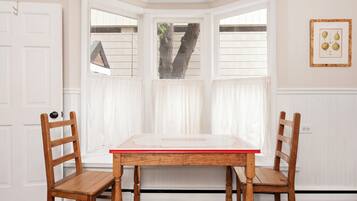 A room with a bay window, two wooden chairs, a table, and a framed picture on the wall.