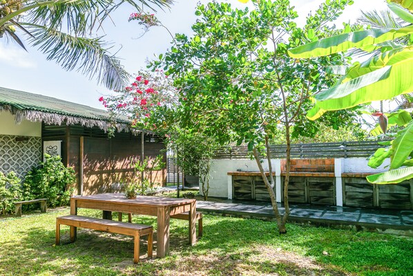 Mesa e banco de madeira num jardim, com uma casa ao fundo.
