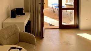 Une pièce dotée d’une porte coulissante donnant sur un espace extérieur, d’un bureau blanc, d’une chaise et d’une télécommande posée sur le sol.