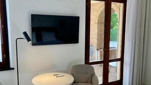 Une chambre moderne équipée d’un téléviseur à écran plat, de deux fauteuils, d’une petite table ronde et d’une porte-fenêtre coulissante donnant sur un espace extérieur.