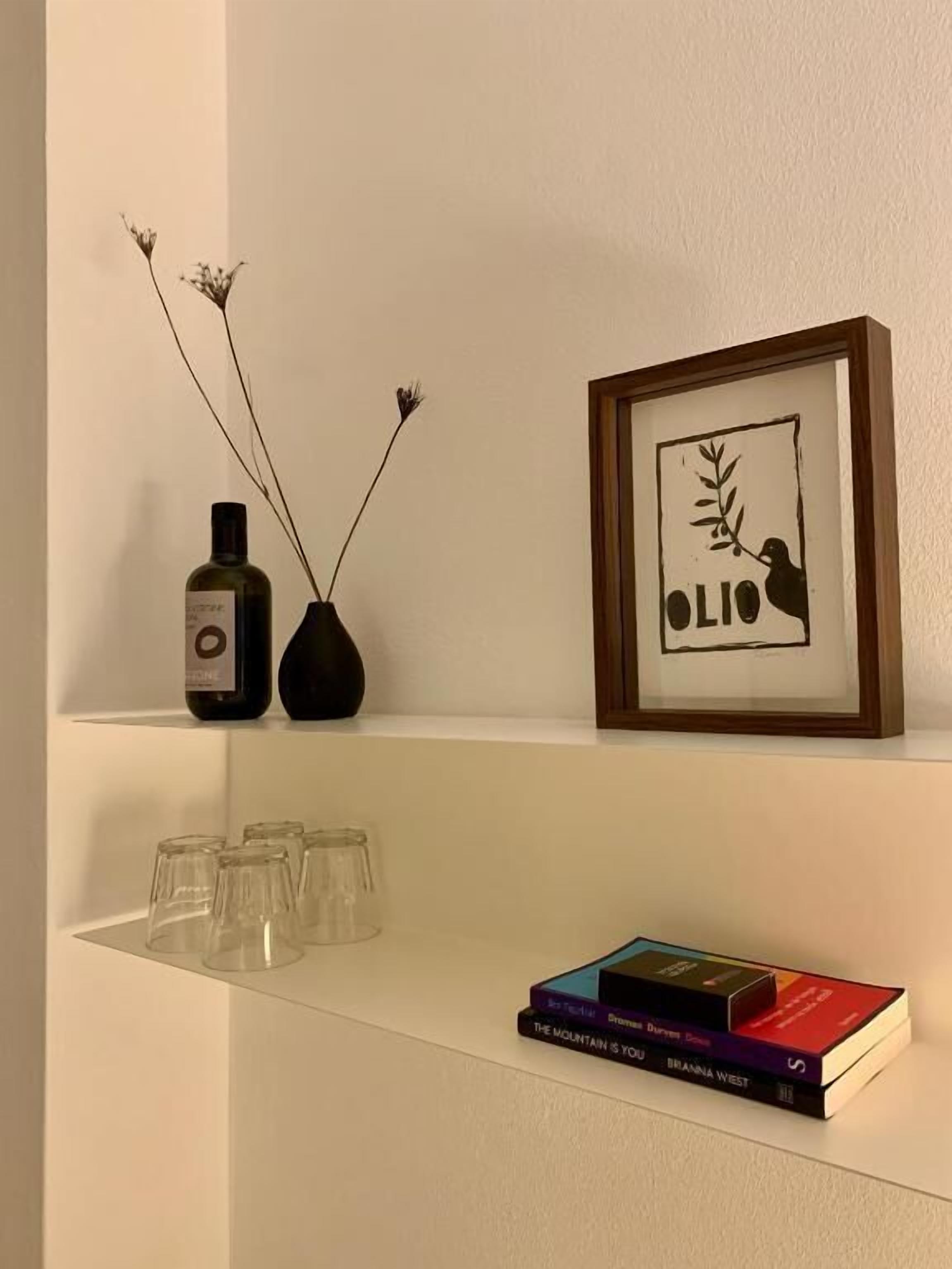 A white shelf with a framed picture, a bottle, and a vase with branches.