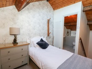 Ein Schlafzimmer mit Bett, Nachttisch, Lampe, Holztür und einem durchgegangenen Tür sichtbaren Badezimmer.