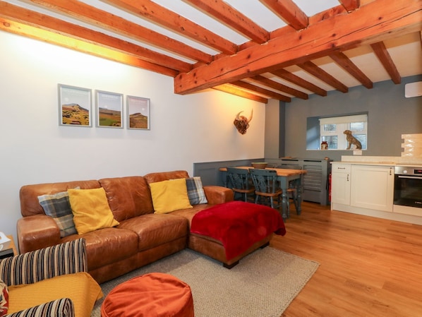 Ein gemütliches Wohnzimmer mit einem braunen Ledersofa, einer roten Tagesdecke und einem Essbereich mit einem Holztisch und Stühlen.