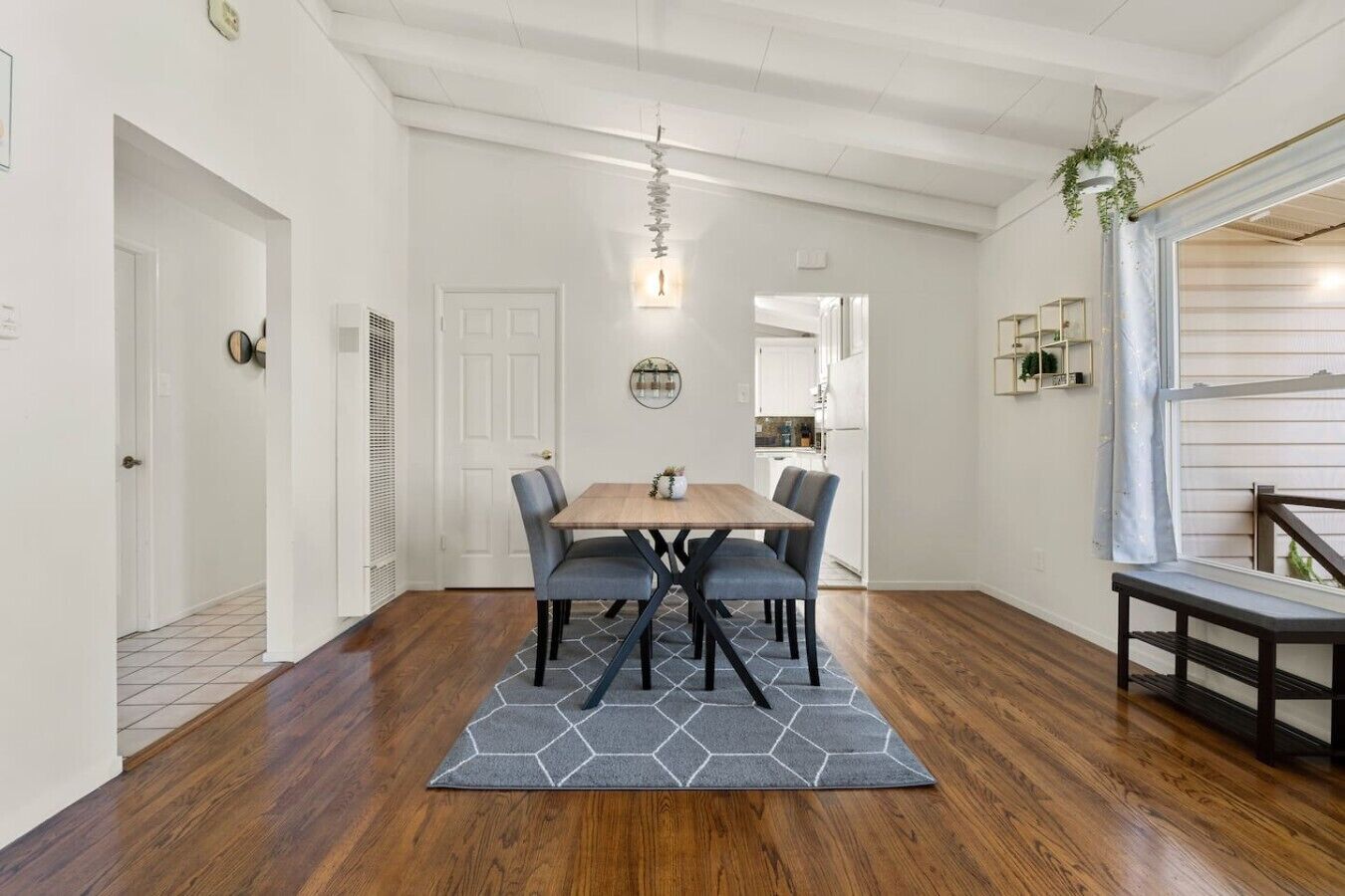 Un comedor con una mesa de madera, sillas tapizadas de color gris, un tapete hexagonal y una lámpara colgante.