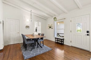 A dining area with a wooden table and chairs, a gray rug, and white walls. - Mid Century Garden View Home Parking (San Mateo)