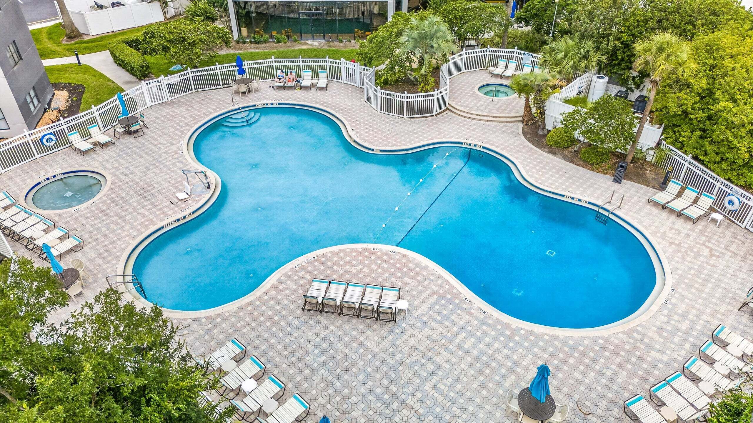 A large, kidney-shaped swimming pool with multiple sunbathing areas and lounge chairs.