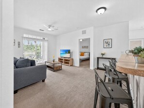 A modern living room with a sofa, TV, and dining area. - Sl102-3176-104-2 - Secret Lake Retreat, Apt. 104 (Kissimmee)