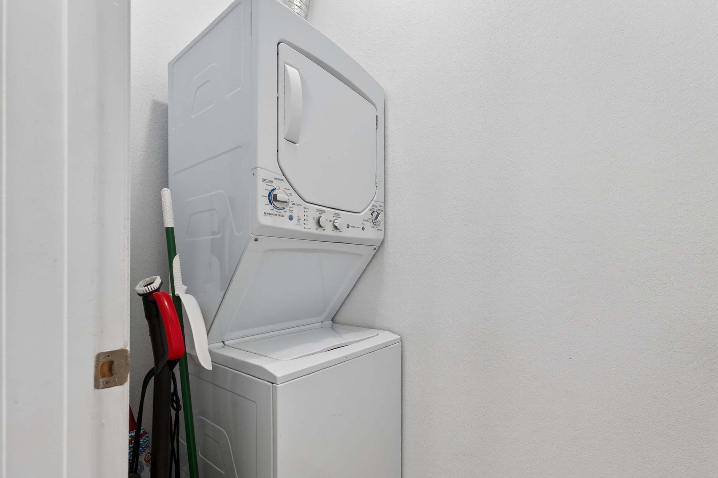 A white washing machine with a door open, a green and red mop, and a white wall.