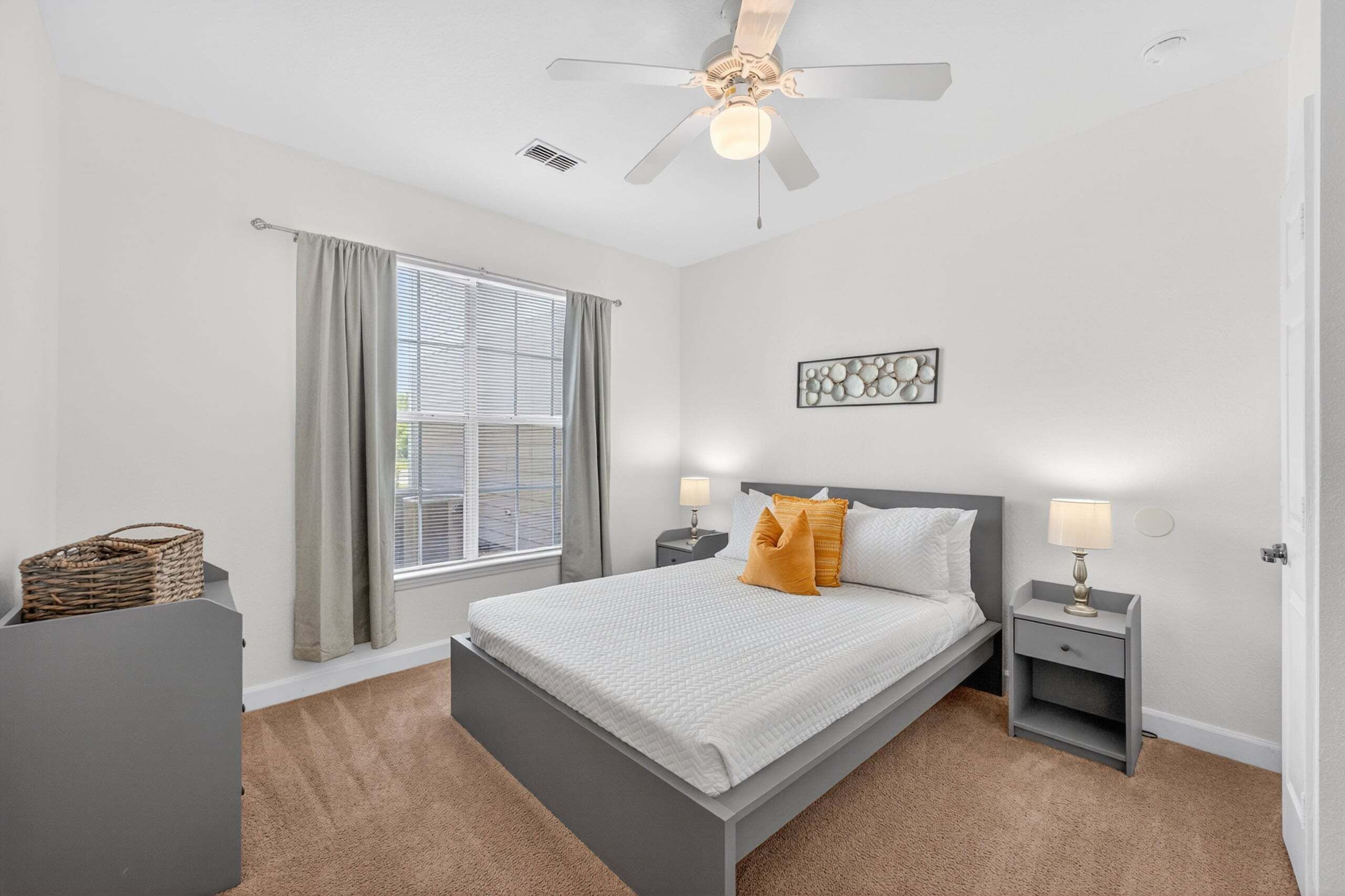 A bedroom with a bed, two bedside tables, a ceiling fan, a window with curtains, and a wall art piece.