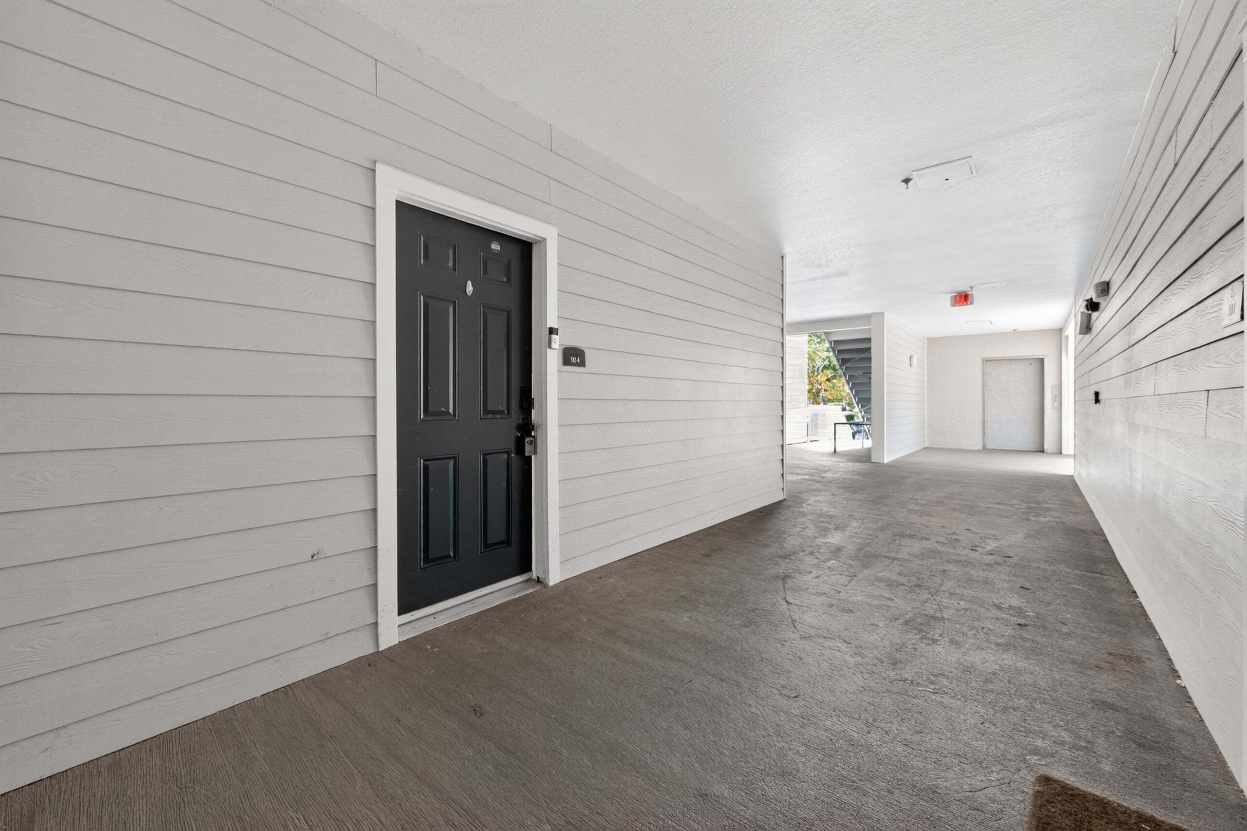 A hallway with a black door, white walls, and a concrete floor.