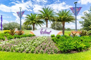 Ein Schild mit der Aufschrift 'Festival' und 'Minto Resorts - Orlando', umgeben von üppiger Vegetation und Palmen.
