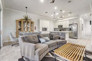 Eine moderne Küche mit weißen Schränken, Edelstahlgeräten und einem Essbereich mit grauem Sofa und einem Holztisch.