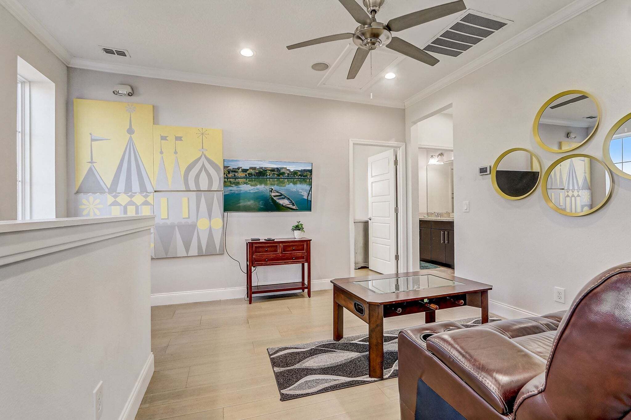 A living room with a sofa, a coffee table, and a TV. There is a painting on the wall and a ceiling fan.