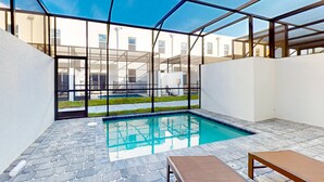 Ein Schwimmbecken mit Glasveranda, Steinboden und einer Liege.