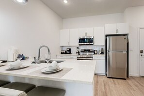 A modern kitchen with white cabinetry, stainless steel appliances, a central island with seating, and a refrigerator. - Two-story Townhouse With Private Pool, Screened Lanai, Washer/dryer (Davenport)