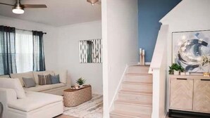 A living room with a sofa, a coffee table, a staircase, and a wall-mounted abstract painting. - The Ultimate Escape at Regal Palms w/ Pool & Lazy River (Davenport)
