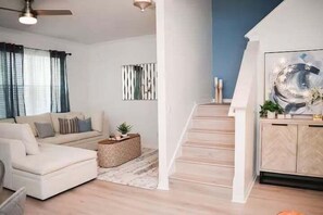 Ein Wohnzimmer mit einer Couch, einem Couchtisch, einer Treppe und einem an der Wand hängenden abstrakten Gemälde.