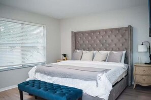 Ein Schlafzimmer mit einem großen Bett, einem Nachttisch mit Lampe und einem Fenster mit Jalousien.