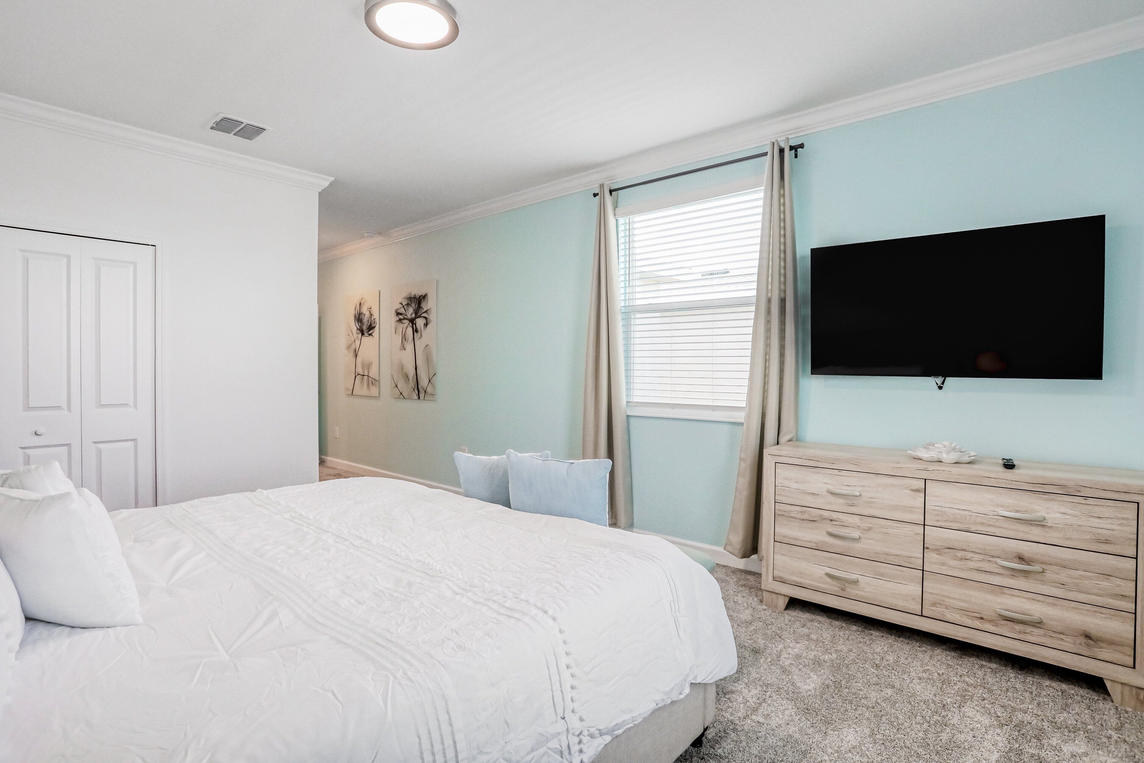 A bedroom with a bed, a dresser, a television, and a window with curtains.