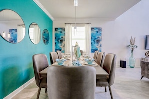 A dining area with a table set for six, surrounded by chairs, with a large mirror and abstract wall art. - All-new, Charming Home With Screened Pool With Spa, Game Room, & Foosball (Davenport)