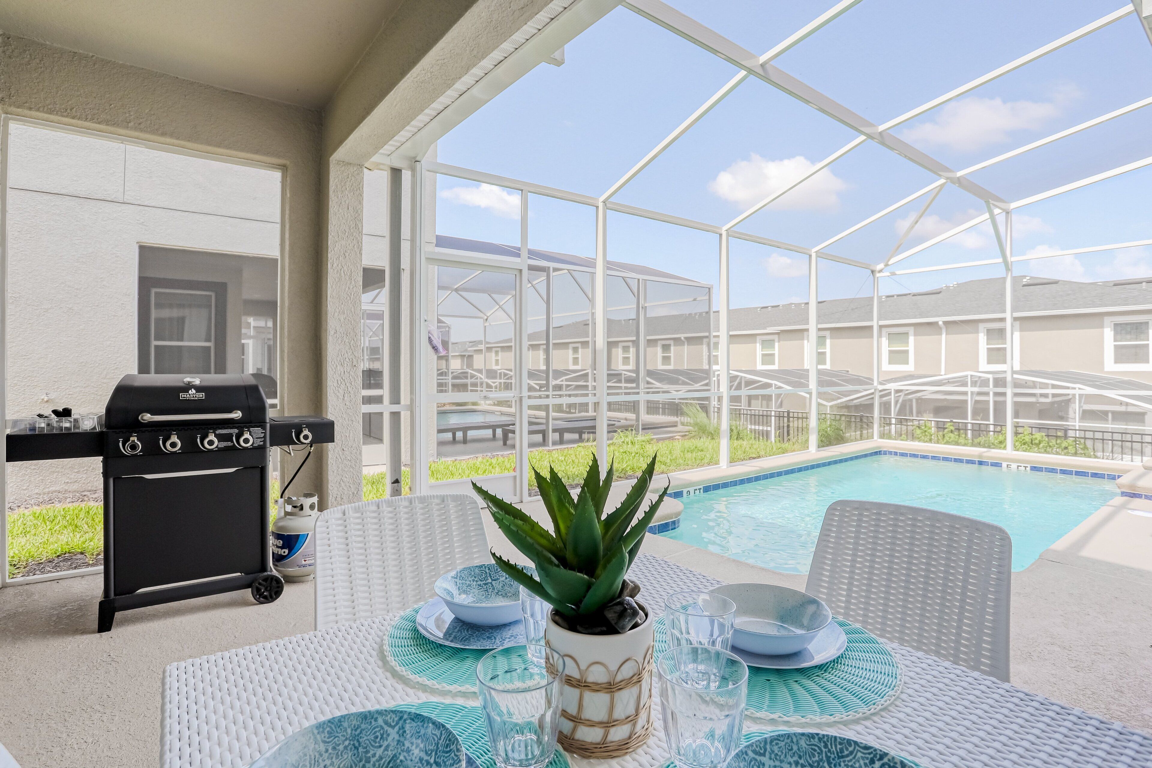 A covered outdoor area with a pool, a grill, and a table set for dining.