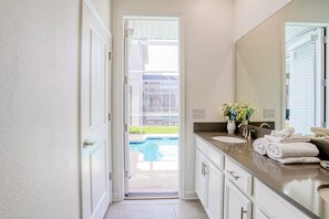 A bathroom with a large mirror, two sinks, and a view of a swimming pool through an open door. - All-new, Charming Home With Screened Pool With Spa, Game Room, & Foosball (Davenport)