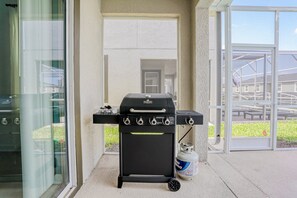 A barbecue grill with a gas tank, positioned near a glass door leading to an outdoor area. - All-new, Charming Home With Screened Pool With Spa, Game Room, & Foosball (Davenport)