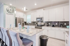 A modern kitchen with white cabinets, stainless steel appliances, a clock, and a dining area with a bench. - All-new, Charming Home With Screened Pool With Spa, Game Room, & Foosball (Davenport)