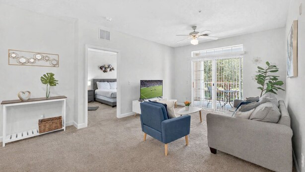 A modern living room with a sofa, armchair, TV, and a balcony with a view. - Peaceful 2BR Pet Friendly Condo Near Disney (Kissimmee)
