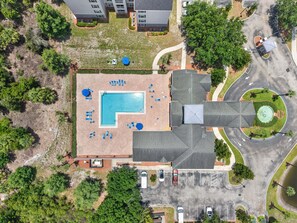 Vista aérea de un hotel con piscina, zona de estacionamiento y follaje circundante.