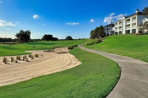 Ein Golfplatz mit einem gewundenen Weg, der zu einem großen Gebäude mit mehreren Balkonen führt.