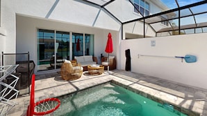 Ein Poolbereich mit Glasveranda, Korbmöbeln und einem roten Sonnenschirm.
