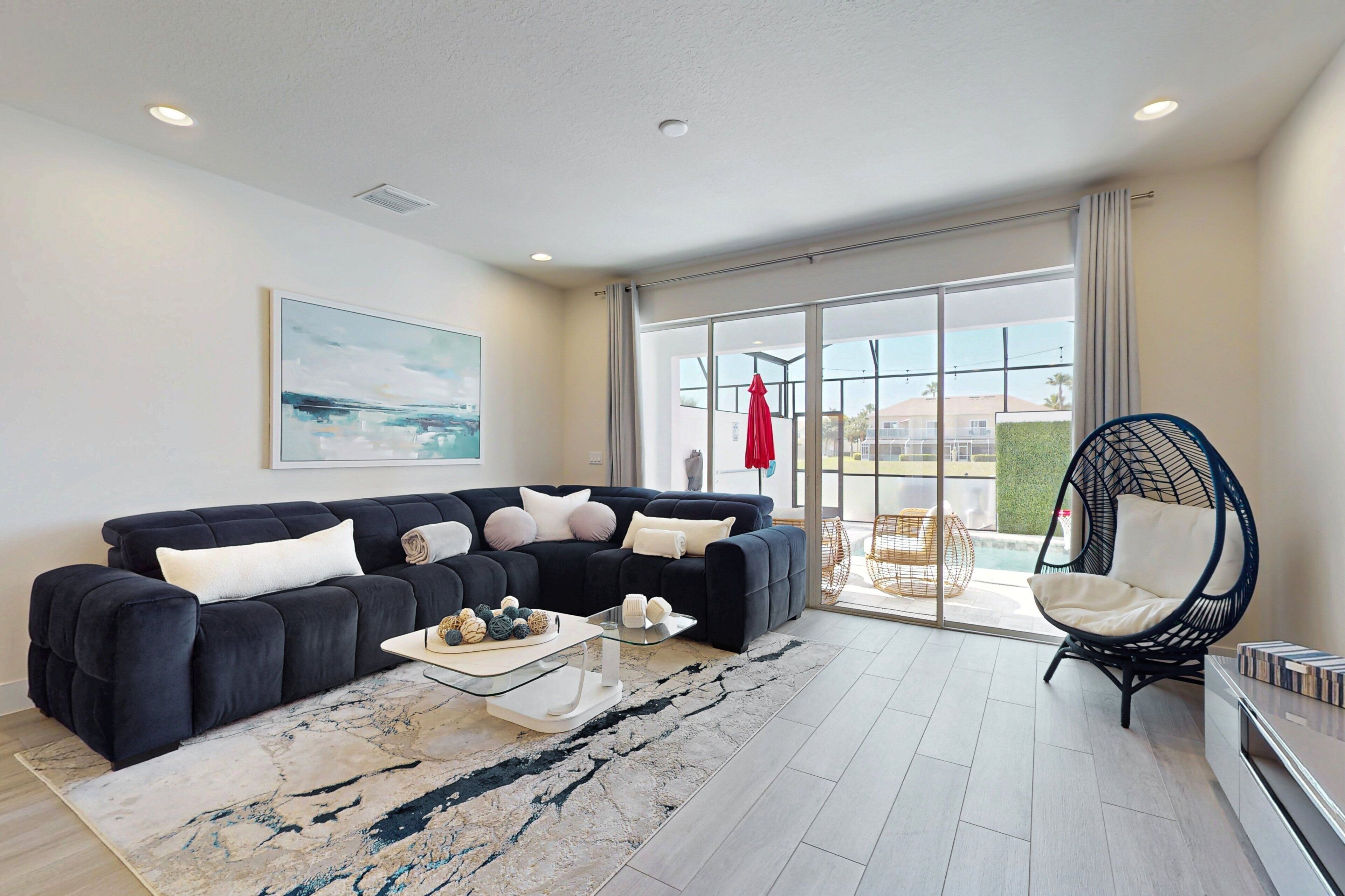 A modern living room with a black sofa, a glass coffee table, and a hanging chair.