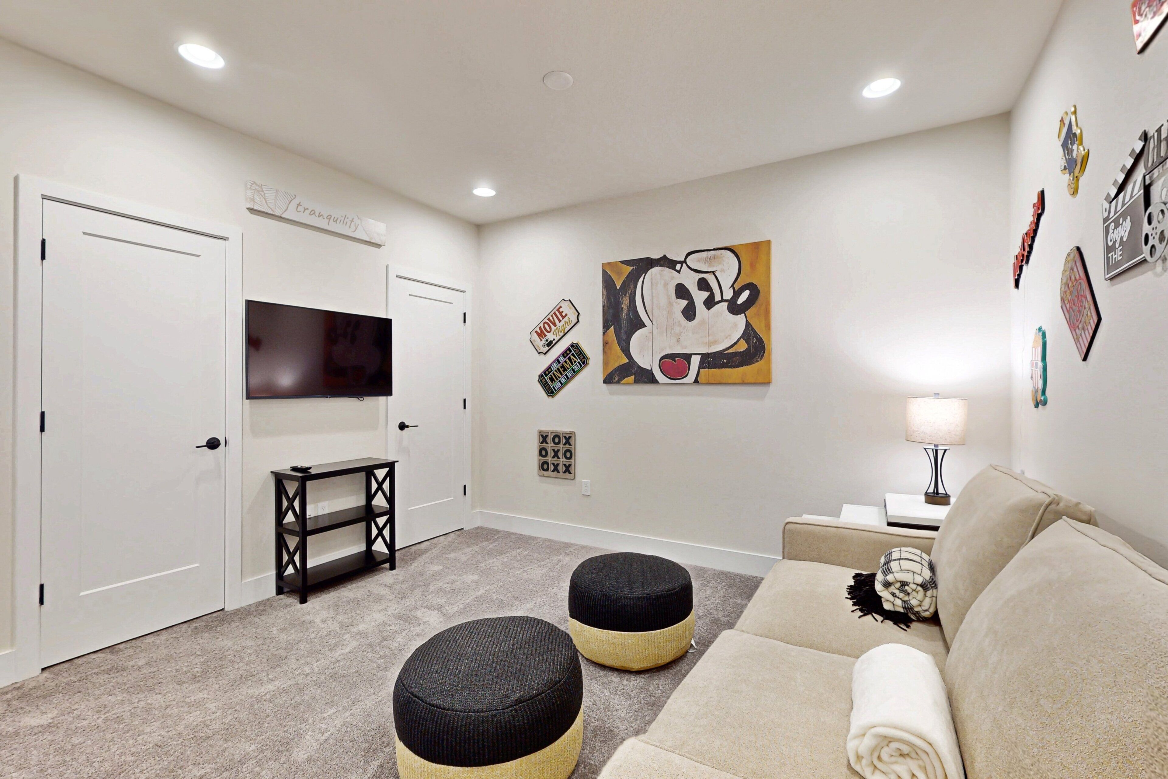 A living room with a TV, ottomans, a sofa, and a wall with movie-themed decorations.