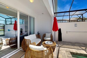 Ein Balkon mit Korbmöbeln, einer Glastür und einem roten Sonnenschirm.