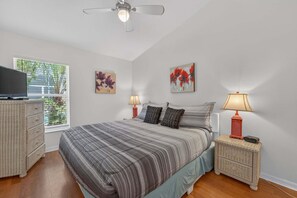 Ein Schlafzimmer mit einem Bett, zwei Nachttischen mit Lampen, einem Deckenventilator und Kunstwerken an den Wänden.