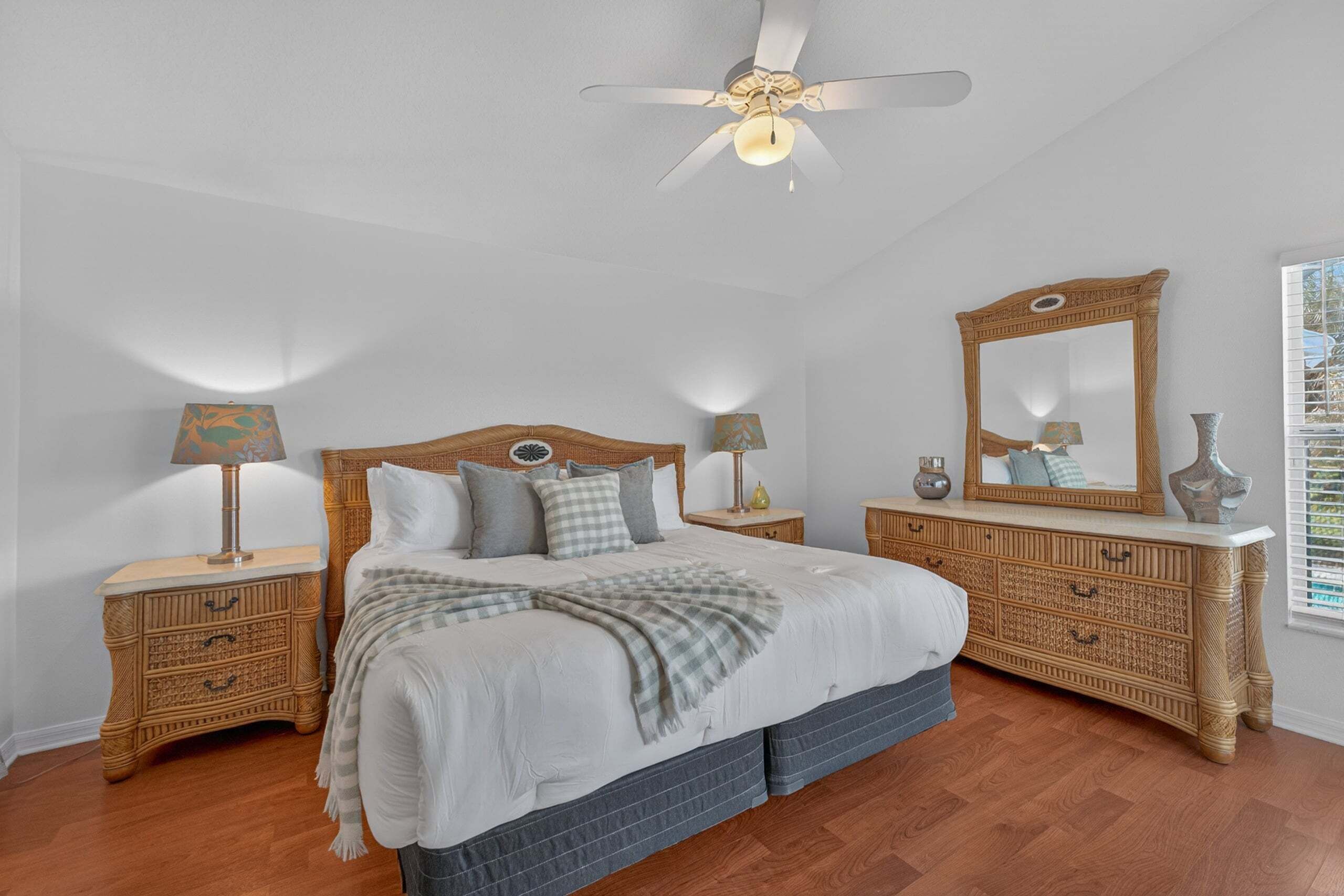 Ein Schlafzimmer mit einem Bett, zwei Nachttischen, einer Kommode, einem Deckenventilator und einem großen Spiegel.
