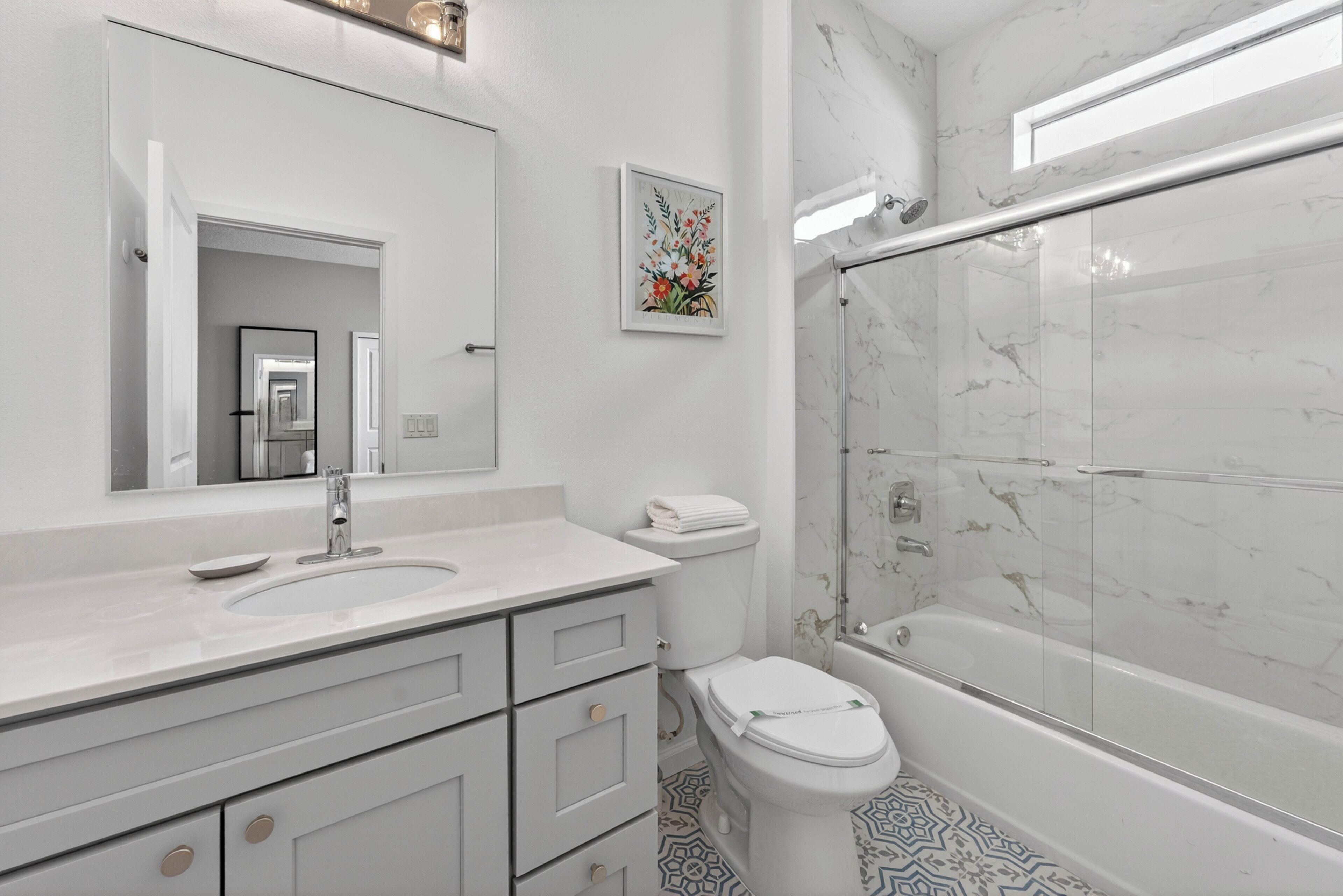 A modern bathroom with a large mirror, a sink, a toilet, and a glass-enclosed shower.