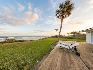 Um deck de madeira com cadeiras de lounge, uma palmeira e vista para o oceano.