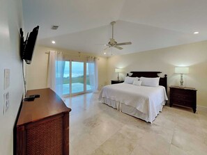 Quarto com cama, mesas de cabeceira, ventilador de teto, TV fixada na parede e vista através da porta de correr de vidro.