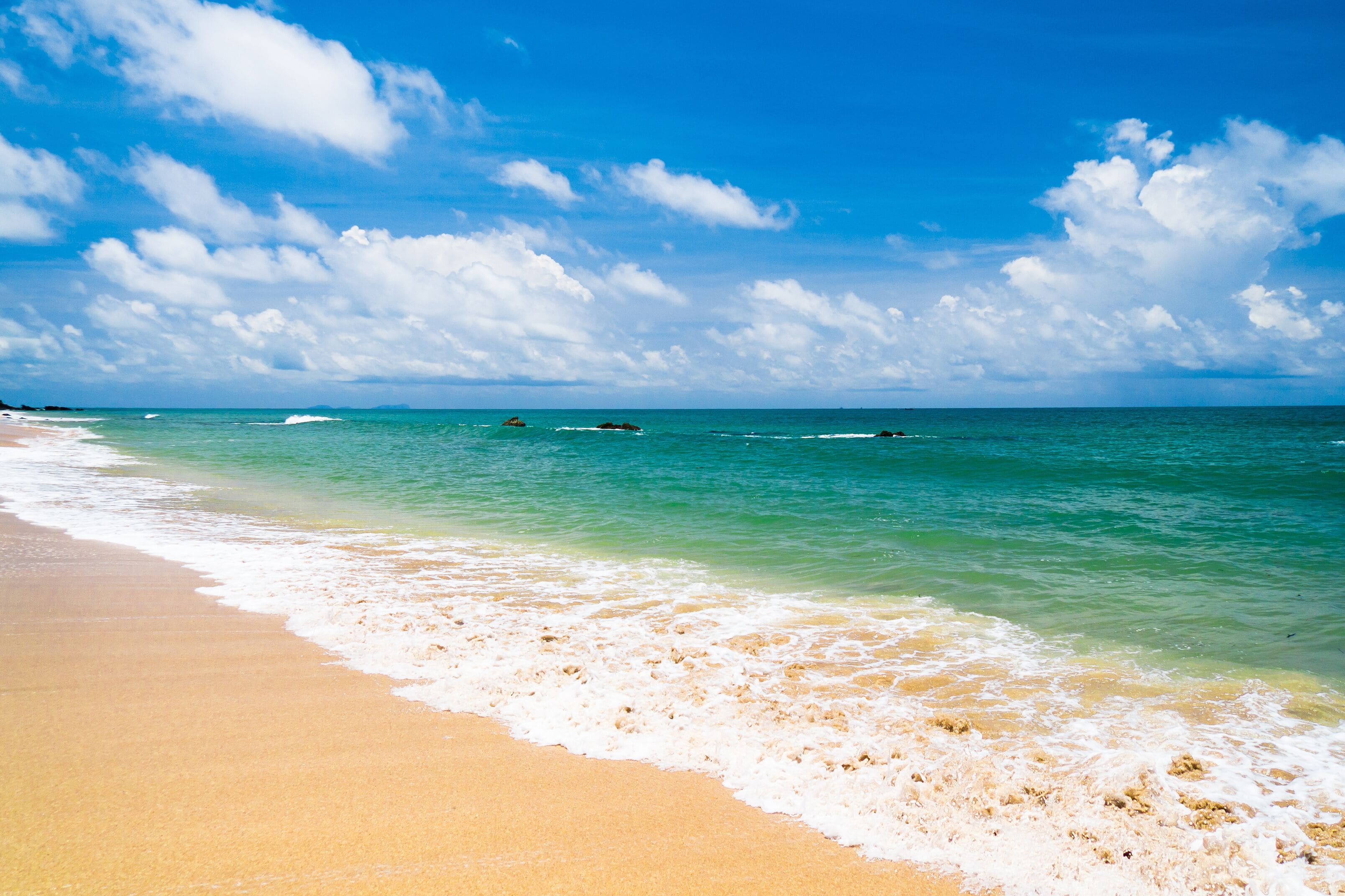 A beach with clear turquoise water, white sand, and a partly cloudy sky.