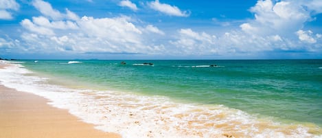 A beach with clear turquoise water, white sand, and a partly cloudy sky.