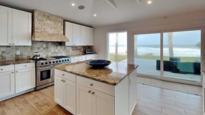 Una cucina moderna con mobili bianchi, una parete di fondo in pietra e un'isola grande.