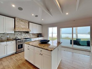 A modern kitchen with white cabinets, a stone backsplash, and a large island. - Ocean Sunrise (Ponte Vedra Beach)