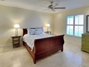 Quarto com cama de madeira, duas luminárias de cabeceira, ventilador de teto, cômoda e janela com persianas.