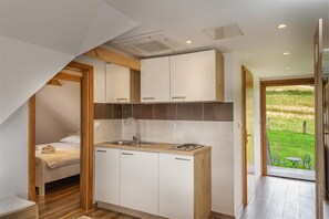 A compact kitchen with a built-in sink, wooden cabinets, and a view of a grassy outdoor area. - Nature Escape With Pool & Garden Views (Ribnik)